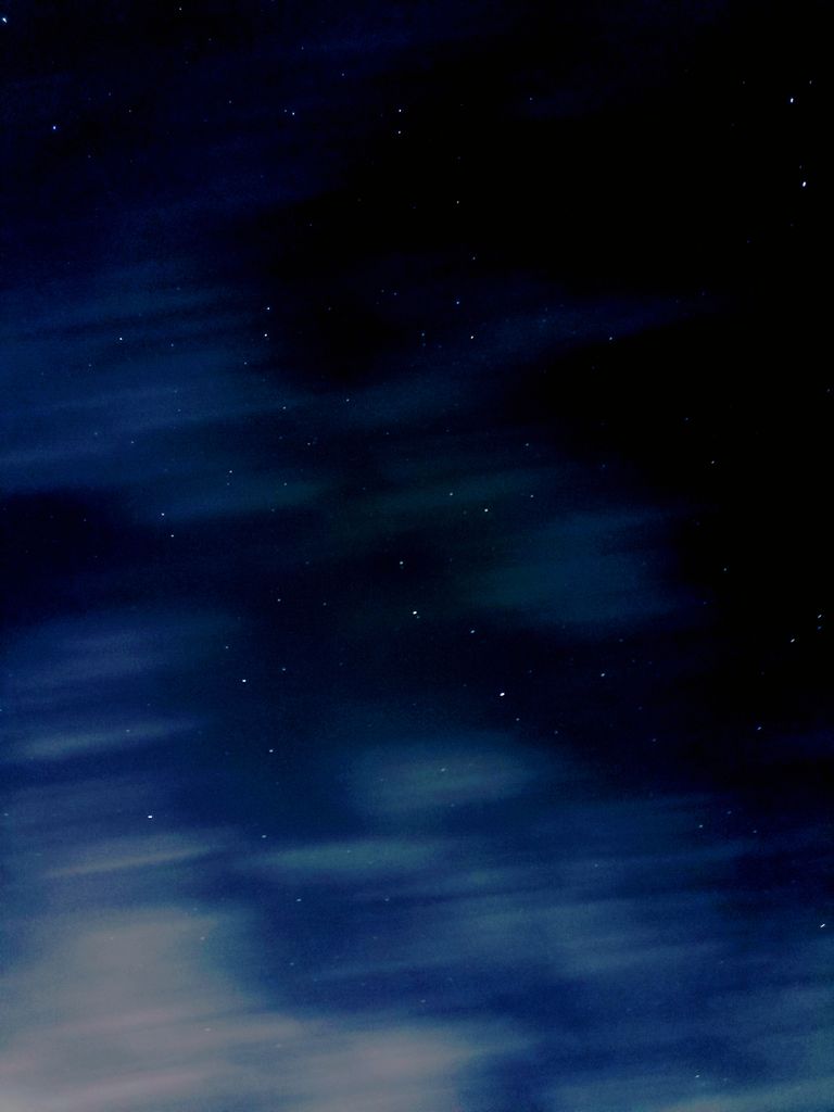 A dramatic capture of the night sky featuring stars and blurred clouds.