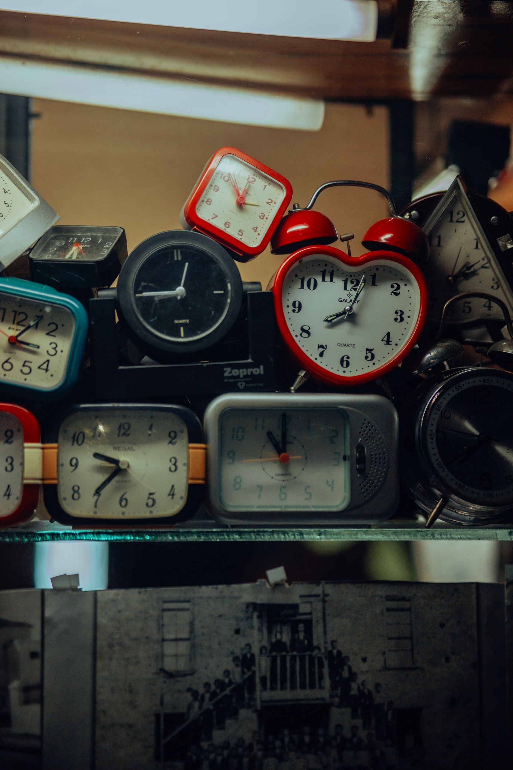 A vintage assortment of various alarm clocks stacked on a shelf, showcasing different styles and colors.