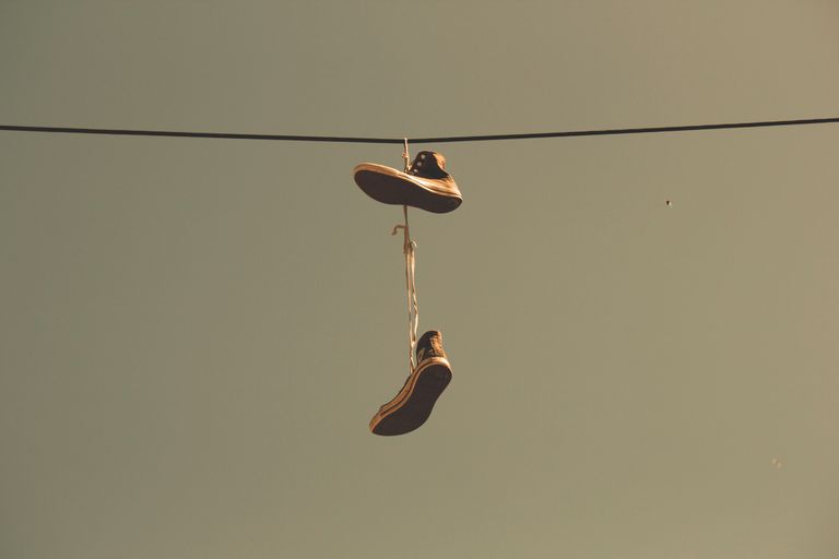 Casual sneakers hanging by their laces on a power line under a clear sky, creating an urban scene.
