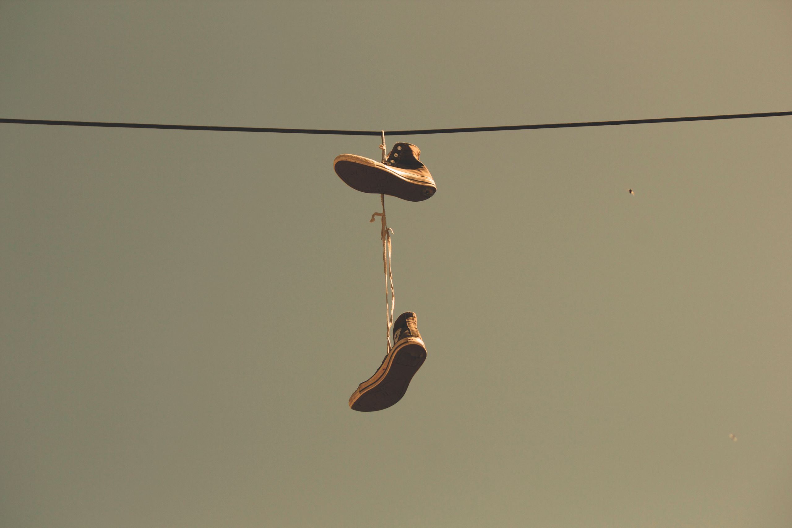 Casual sneakers hanging by their laces on a power line under a clear sky, creating an urban scene.